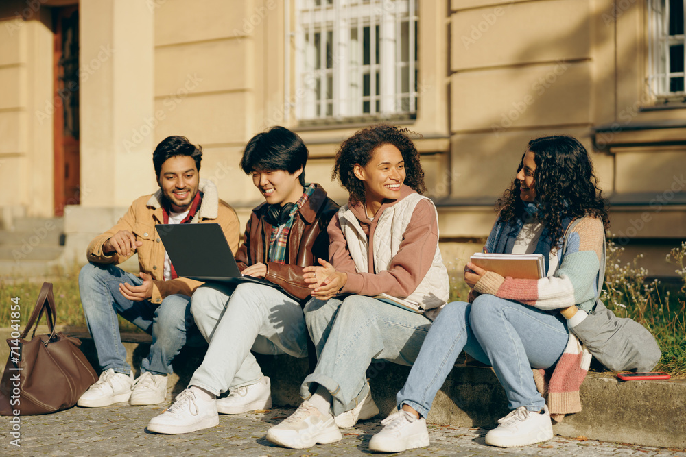 Happy students sitting outdoors, looking at laptop and discussing their project together