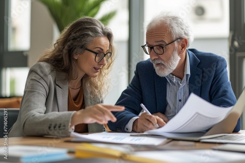 Two professional executives discussing financial accounting papers working together in office. Mature business woman manager consulting older man client holding legal documents at meeting