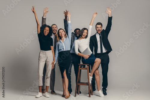 Happy young business team in formalwear gesturing while standing on beige background