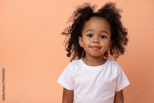 design mockup black toddler girl wearing plain blank white tshirt on a pastel peach background, studio portrait