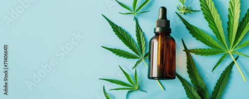 A brown dropper bottle with CBD oil surrounded by green cannabis leaves on a blue background, suggests health, wellness, and natural alternatives in personal care. Banner with copy space. photo