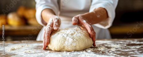 A baker kneads dough on a floured surface, preparing it for baking fresh bread. Hands-focused, bakery atmosphere, culinary craftsmanship at work. Banner with copy space. photo