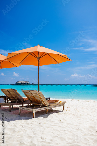 Outdoor tourism landscape. Luxury beach resort closeup beach chairs or beds under umbrellas with palm trees, sea sand blue sky. Summer leisure travel vacation background. Colorful sunny coast relax 