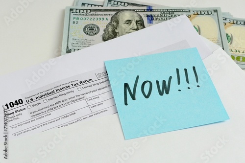 US Tax Form 1040 document in an open envelope and dollar bills on the table. The concept of motivation to start paying taxes now, without delaying until later photo