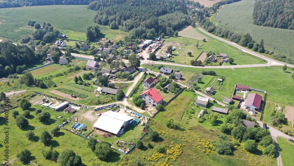 Drone captures a village with cottages, private houses, plots and allotments in Eastern Europe in summer in the middle of a green forest. A typical village in Eastern Europe. Rural roads made of sand.