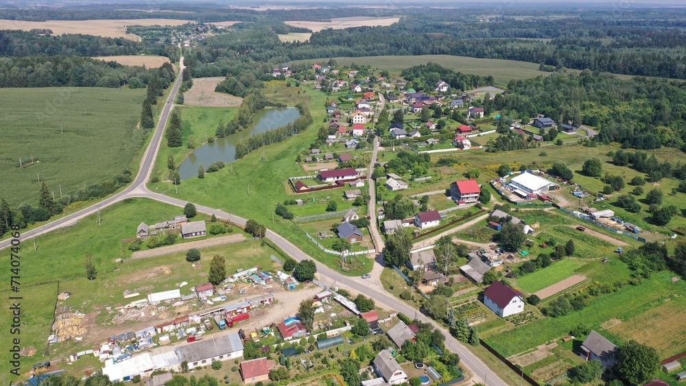 A crossroads, a fork in a village that stands in a green valley surrounded by forest. Aerial view of a European village with one-story houses, cottages. Land plots, personal plots of farmers.