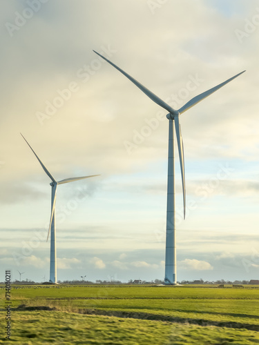 Tall green energy wind mills or turbines at farm, at grassland field
