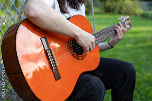 Woman playing acoustic guitar in the garden. Closeup of female hands.