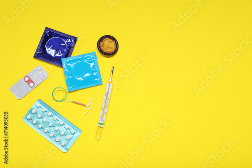 Contraceptive pills, condoms, intrauterine device and thermometer on yellow background, flat lay and space for text. Different birth control methods
