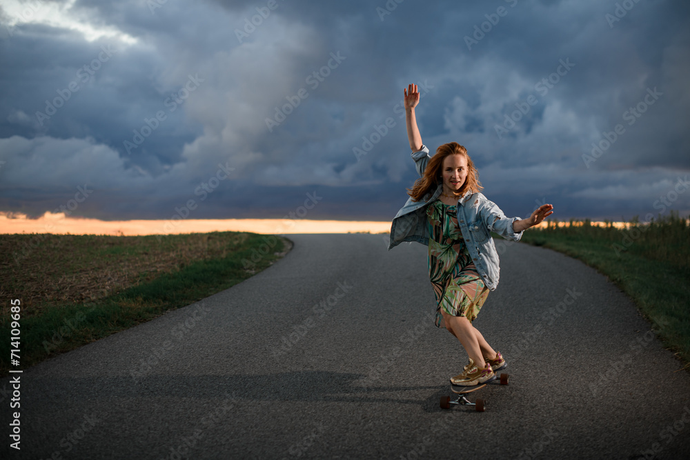 Fototapeta premium Young girl rides in the middle of the road on her longboard with her arms out to her sides for balance
