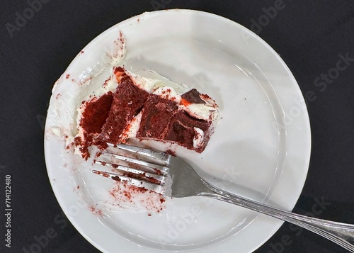 Partially eaten piece of red velvet cake on a white plate with fork