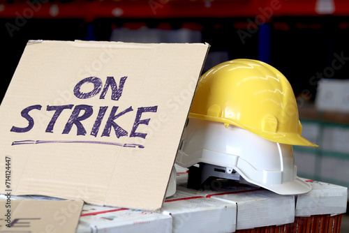 On strike banner placard with two white and yellow worker helmets at cargo logistic warehouse. Striking worker protesting and do not to work at workplace, symbol of strike concept. photo