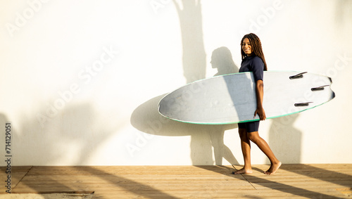 Photography A woman walks near a wall with a surfboard dressed in a wetsuit
