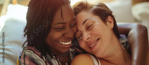 Joyful lesbian woman embracing expectant multiracial spouse at home, their faces beaming. photo