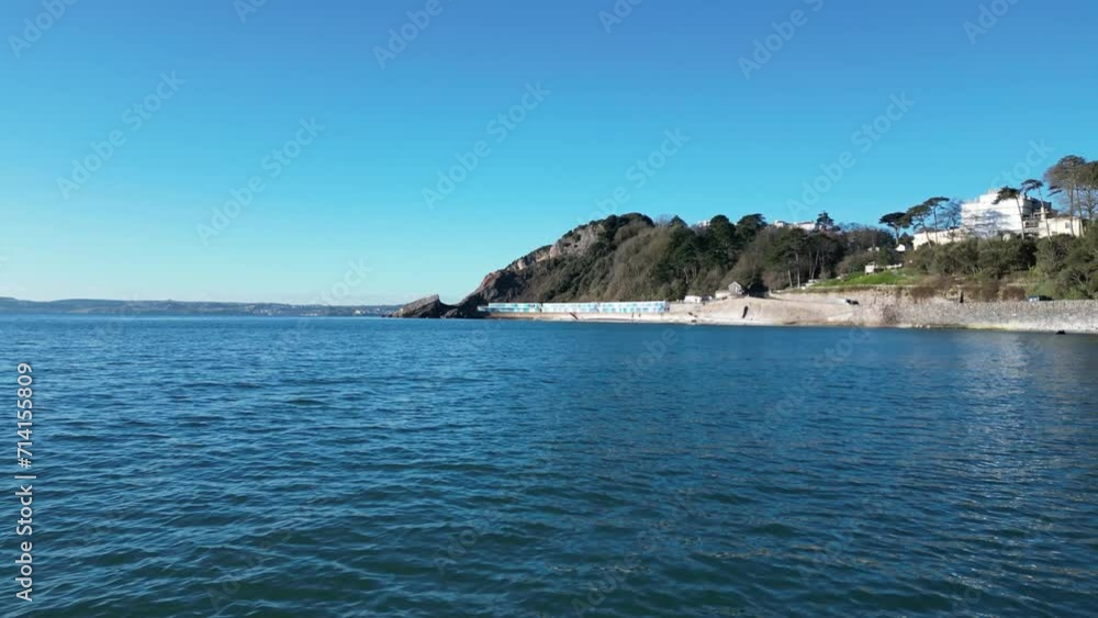 Meadfoot beach, Torbay, South Devon, England: DRONE VIEWS: Low angle view of the sea, offshore rocks and chalets on Meadfoot beach, which is close to the popular UK holiday resort of Torquay (Clip 3). Meadfoot beach, Torbay, South Devon, England: DRONE VIEWS: Low angle view of the sea, offshore rocks and chalets on Meadfoot beach, which is close to the popular UK holiday resort of Torquay (Clip 3).