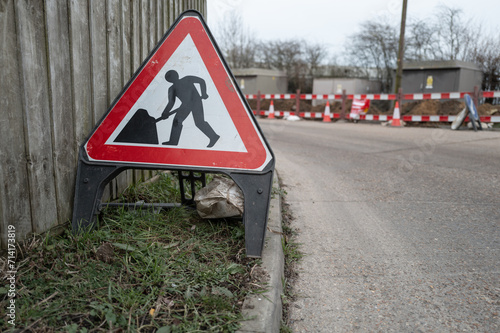 Shallow focus of a British road works sign seen on a grass verge at a dangerous road corner. Gas pipes are being laid.