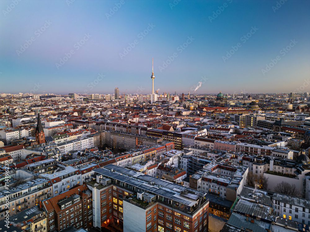 Aerial panoramic shot of apartment houses in Mitte district at twilight. Popular tall Fernsehturm in distance against clear sky. Berlin, Germany