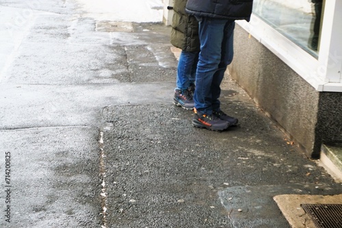 Ehepaar steht auf schneebedecktem Gehweg vor Schaufenster von Laden in Stadt bei Kälte, Frost und Schnee am Nachmittag im Winter