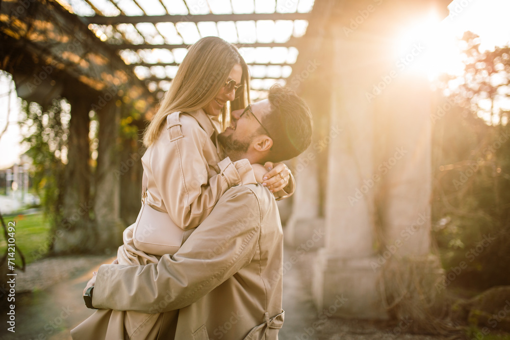 Close-up shot of a beautiful couple posing in a park garden on a spring sunny day. A man holds a woman in his arms. Family, love and happiness concept. - obrazy, fototapety, plakaty 