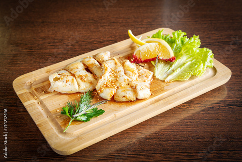 Grilled squid with lemon and lettuce on a wooden board.