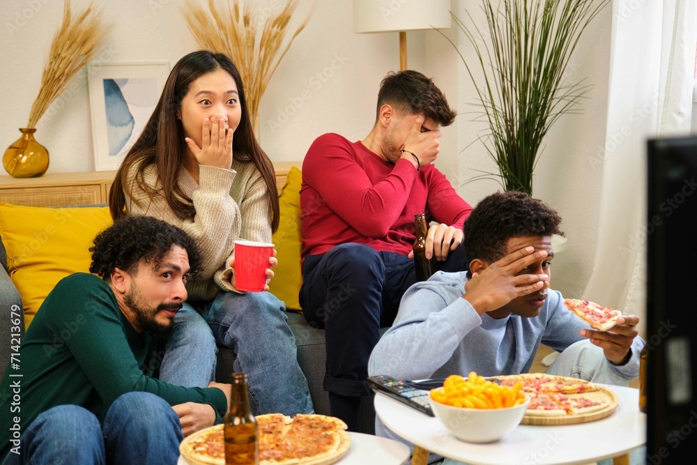 Group of friends eating pizza and watching a horror movie in a shared student house.