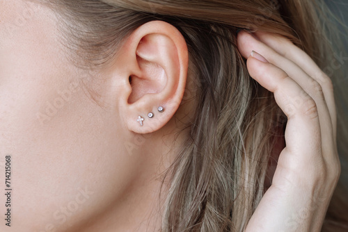 Ear piercing. Cropped shot of a young woman wearing three stud earrings on the earlobe. Jewelry with gemstones, accessories, a cross with fianits photo