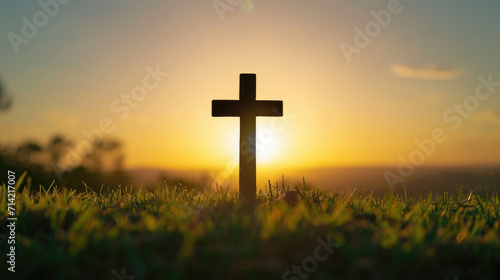 Silhouette cross at sunrise on grass.