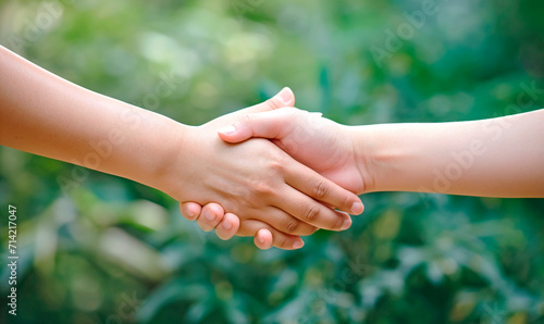 Handshake on a green background. Blurred nature background. Two hands reach out to each other. The concept of friendship and mutual assistance. Support. Help. © Honey Bear