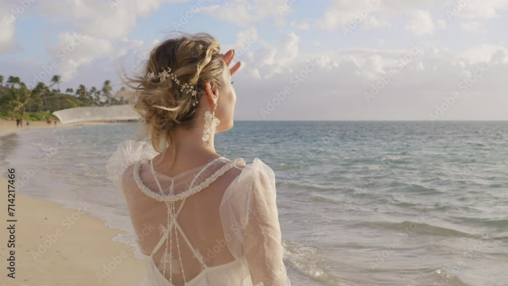 Young woman in fashionable trendy boho style white sheer floral wedding dress looking at ocean. Back view of romantic bride standing on tropical beach. Beach wedding, bright future, honeymoon vacation Young woman in fashionable trendy boho style white sheer floral wedding dress looking at ocean. Back view of romantic bride standing on tropical beach. Beach wedding, bright future, honeymoon vacation