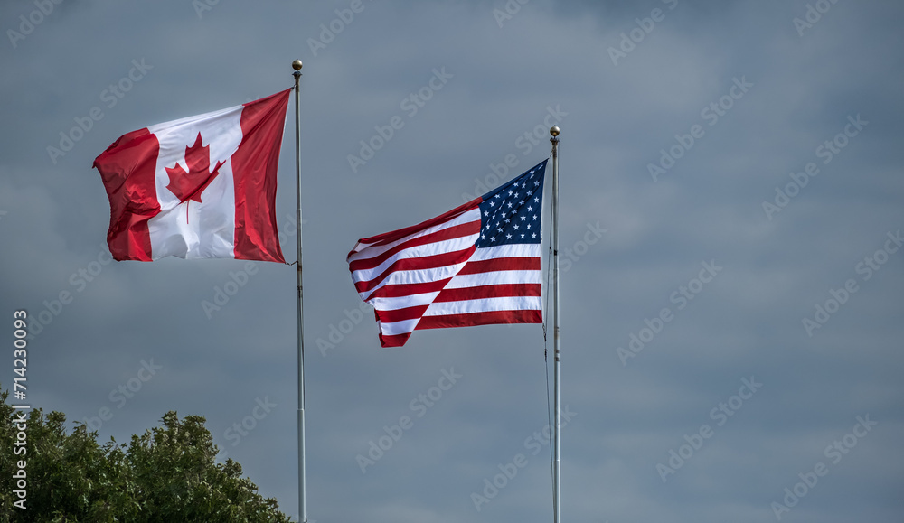 American and Canadian flags together. American and Canadian flags flying side by side at the border between USA-Canada American and Canadian flags together. American and Canadian flags flying side by side at the border between USA-Canada