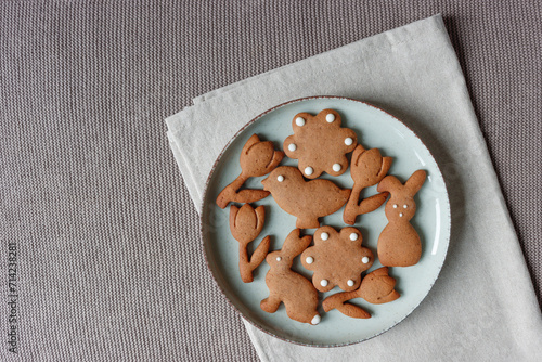 Osterkekse auf Keramikteller, liegend auf beiger Baumwollserviette und einem taupe-farbenen Strick-Tischset