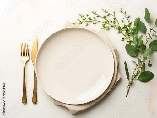 Festive table setting with gold cutlery, a porcelain plate and a green plant. View from above