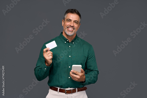 Happy middle aged business man, smiling mature businessman holding mobile phone and credit debit card mockup using banking finance app making online purchase on smartphone isolated on gray background. photo