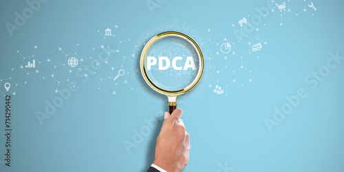 PDCA: Businessman Hand Holding a Magnifying Glass with Plan-Do-Check-Act (PDCA) Icon on Light Blue Background. Continuous Improvement, Quality Assurance, Process Optimization. photo