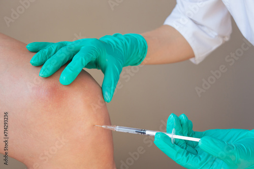 A doctor in green gloves gives a young man an intra-articular injection of hyaluronic acid against osteoarthritis in the knee joint. Preventing the destruction of the knee joint.