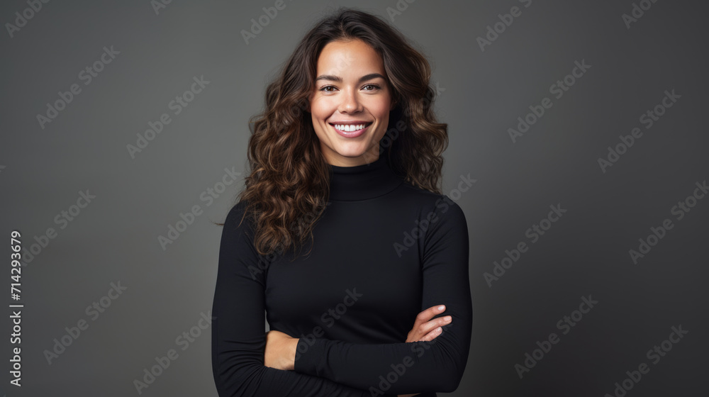 Woman with curly hair is smiling and posing confidently with her arms crossed, wearing a black turtleneck against a neutral gray background. Woman with curly hair is smiling and posing confidently with her arms crossed, wearing a black turtleneck against a neutral gray background.