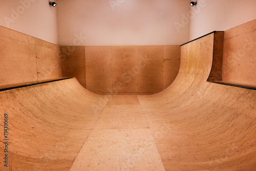 An indoor skateboard sports ramp / halfpipe lit by spotlights with no people, wooden texture and wooden & plaster walls, symmetrical and minimal composition. underground skate social / competition