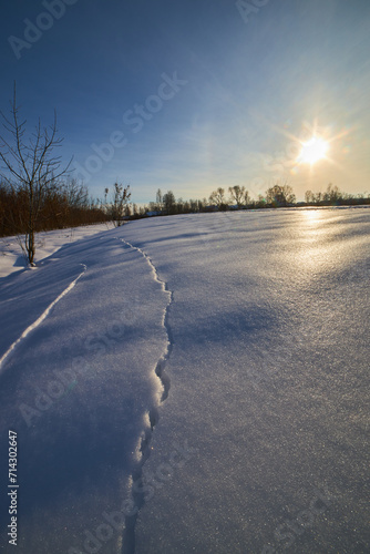 Frozen crust of ice on snow  present. Winter landscape with snow fields and sun.