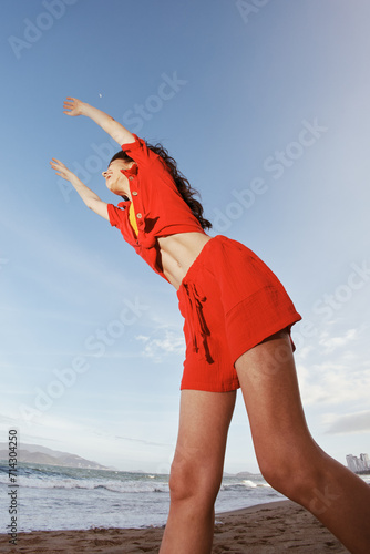 Fototapeta Naklejka Na Ścianę i Meble -  Smiling woman enjoying the freedom of beach vacation: Joyful Dance in Red Clothes under the Sunny Blue Sky