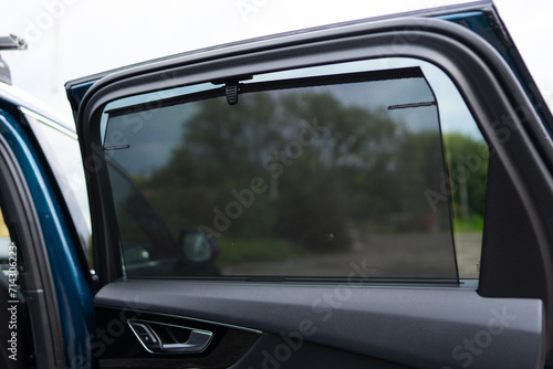 Rear window sunshade providing additional protection for back seat passengers of expensive auto. Adjustable fabric screen blocking light and heat from cabin © port-o