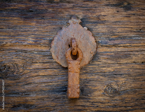 Ancient door knocker on wooden door .