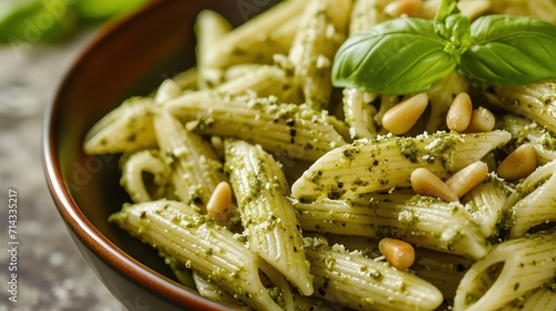  a close up of a bowl of pasta with pesto and pine nuts on the top of the pasta and garnished with a sprig of basil.