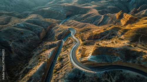  an aerial view of a winding road in a mountainous area, with a view of a valley and mountains in the distance, taken from a bird's eye angle.