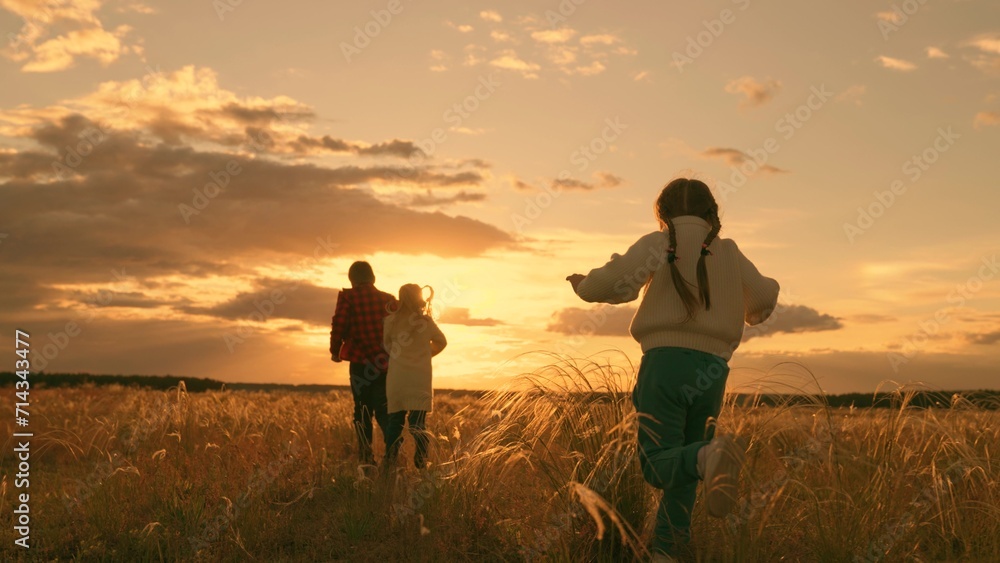 Children run together in park at sunset on grass. Happy family, teamwork. Running children, boy, girl, dream of flying, raise your hands like an airplane. Children play in sun, flight, freedom, nature