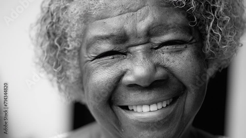 One happy black senior woman in 80s in black and white. Monochromatic portrait of wise older African American lady smiling at camera showing old age and wisdom