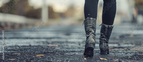 Black-jeaned woman walking on city pavement. Female feet in worn boots and tattered pants. © 2rogan