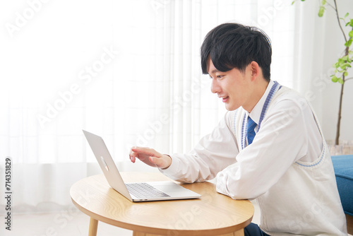 リビングでノートパソコンで動画を見る男子高校生 photo
