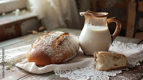  a loaf of bread sitting on top of a table next to a jug of milk and a loaf of bread on top of a doily cloth on a table.