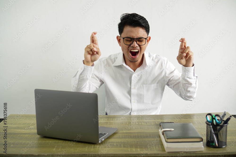 angry young asian businessman in a workplace with finger crossing, wearing white shirt with glasses isolated angry young asian businessman in a workplace with finger crossing, wearing white shirt with glasses isolated