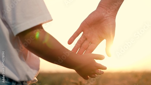 Dad and preschooler son stand hand in hand in warm glow of setting sun. Parent and kid walk together surrounded by beauty of nature. Child spends time with dad and shares peaceful moment in open field photo